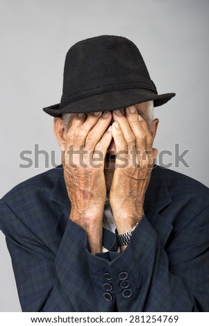 Portrait of a sad old man covering his face with hands over gray background