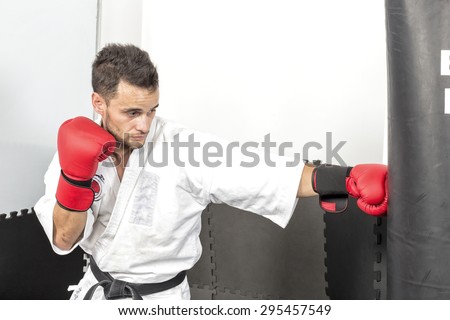 Young man in kimono throwing punches at a heavy punching bag during his training