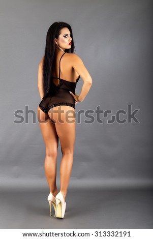 Full length portrait of beautiful brunette woman posing in sexy black lingerie and high heels over gray background