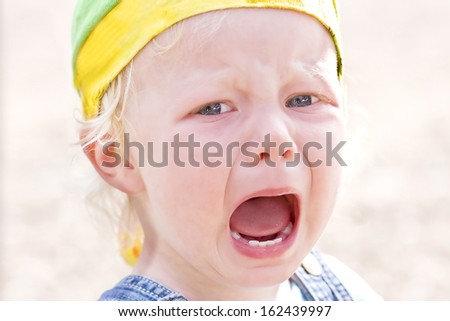 Close-up on a blond baby girl bawling furiously (focus on the left eye and the mouth).