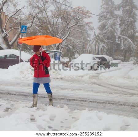 JERUSALEM - FEBRUARY 20: Woman walking under the snowfall with a broken orange umbrella during a massive snowfall in Jerusalem on February 20, 2015