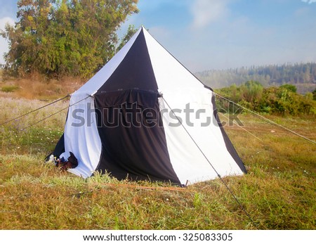 Large black and white medieval pavilion tent at sunset meadow