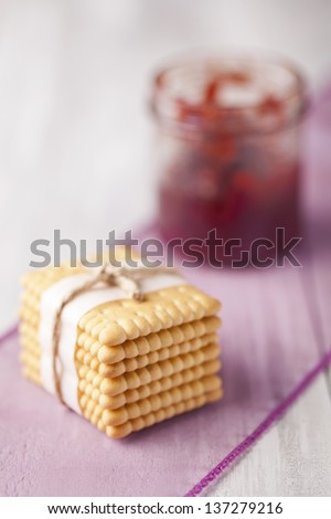 Stack of fresh baked biscuits tied with vintage string and jar of red fruit jam. Sweets composition taken on white table.