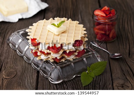 Traditional homemade fresh baked waffles served with strawberries and whipped cream. Dessert and fresh ingredients composition.