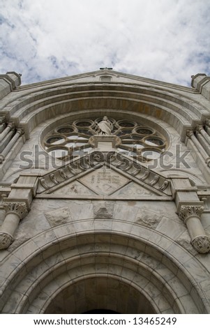 Front facade of a gothic church with rosette window and statuette from steep angle also showing arch of doorway