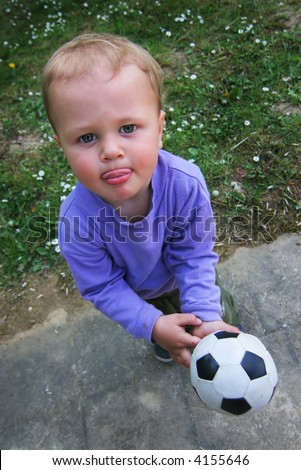Child is holding ball in his hand and sticking out his tongue