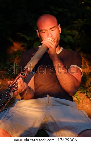 Young guy play on didgeridoo with the australian aboriginal musical instrument in lights of sunset