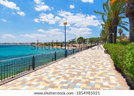 Picturesque seafront promenade of Punta Prima. Empty fenced  pedestrian walkway and turquoise Mediterranean Sea. Costa Blanca, Spain. Summer vacation, travel and holidays concept Stockfoto © 