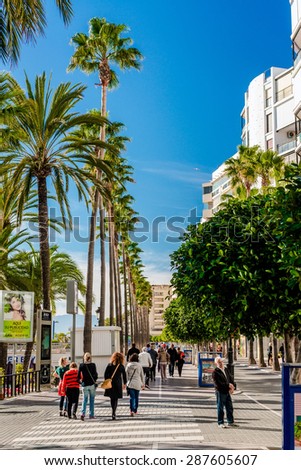 Marbella, Spain- January 8,2014: Crowd of people walking along the seafront promenade in sunny winter day. Marbella resort city. Malaga, Costa del Sol. Southern Spain