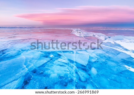 Blue ice of Baikal lake under pink sunset sky
