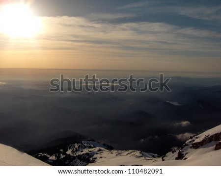 Long range vistas as viewed from the top of Mt. Hood in state of Oregon in the United States of America with snow on rocky boulders, blue skies, wispy clouds and sunshine