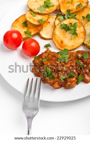 roasted country-styled potatoes with meat tomato sauce and two cherry tomatoes on a white plate and a fork