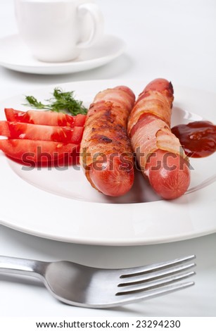 vienna sausages wrapped in bacon, sliced tomatoes and ketchup on a white plate with espresso coffee in the back