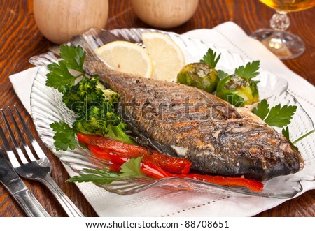 Dorado fish garnished with vegetables, herbs and lemon  on a dish