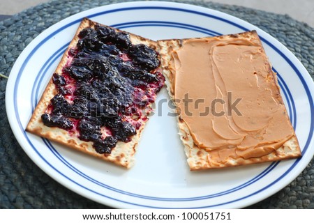 Leftover Matzohs. Two pieces of after Passover matzohs covered in peanut butter & jelly arranged on white porcelain plate.