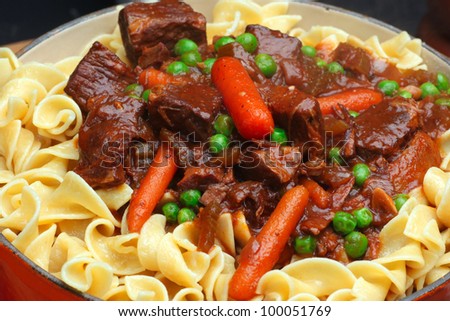 Beef Stew with Carrots & Peas. Close up of beef stew in dutch oven made with top round, baby carrots, green peas & served over a bed of egg noodles.