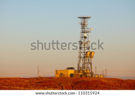 Red Sand Blue Sky/Long view of transmission tower along Route 66 amid reddish sands of New Mexico desert.