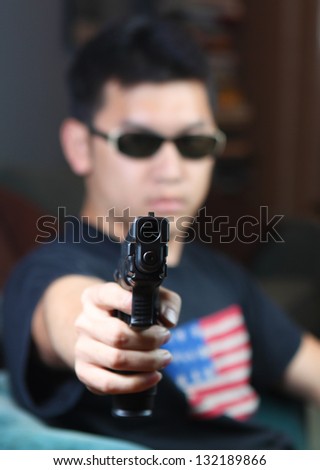 A Dangerous Fellow/Soft focus view of sunglasses-wearing Chinese man pointing automatic pistol at viewer, with focus on gun barrel
