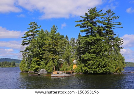 Small island in Moosehead Lake, Maine, with wood cabin, thick foliage & rustic wood dock