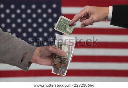 American Gothic Series/Suited man\'s hand about to place dollar bill into panhandler\'s cup with out of focus US flag in the background