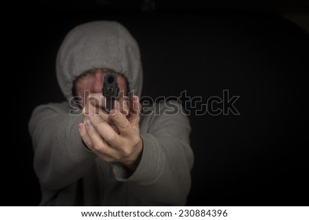 Middle age man in gray hoodie pointing handgun at camera, focus on gun barrel, with dark background