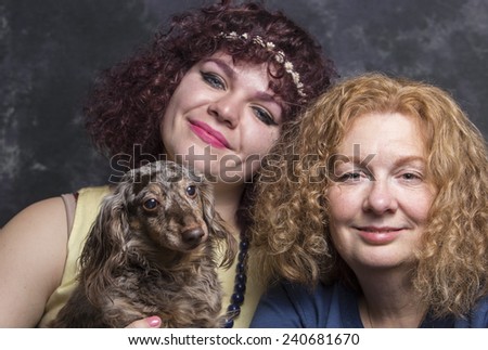 Two women with red hair posing against portrait background while holding small dogs