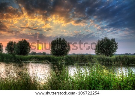 Beautiful vibrant HDR river sunset with clouds and willows at the river Angstel in the Netherlands