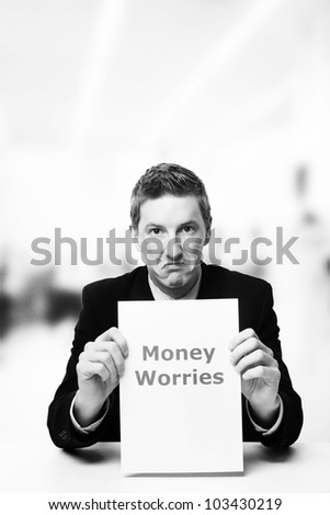 man in a suit sat at a desk look at a  piece of paper with the words money worries printed on it