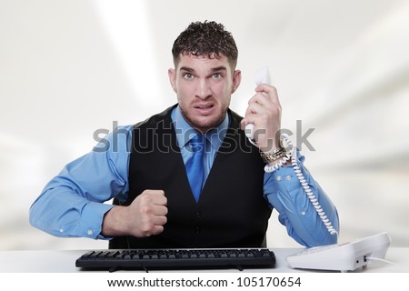 stress out business man siting at his desk banging fist against a computer keyboard with one hand and in the other he is holding a telephone with the cord twisted around his arm.