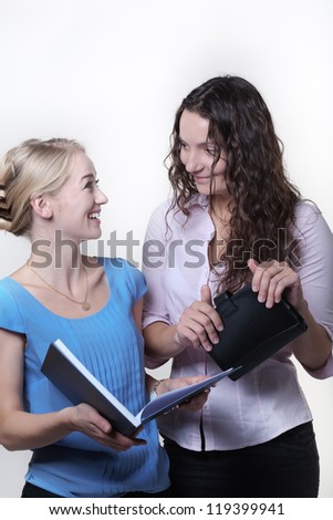 two work colleagues looking over something in a large note book, one woman is laughing out loud having fun