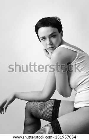 sexy woman wearing a vest top siting down on a chair wearing fishnet hold ups