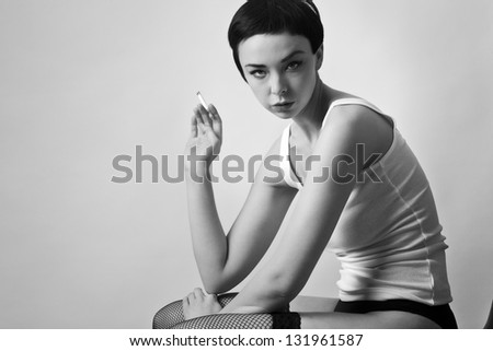 sexy woman wearing a vest top siting down on a chair wearing fishnet hold ups smoking a cigarette