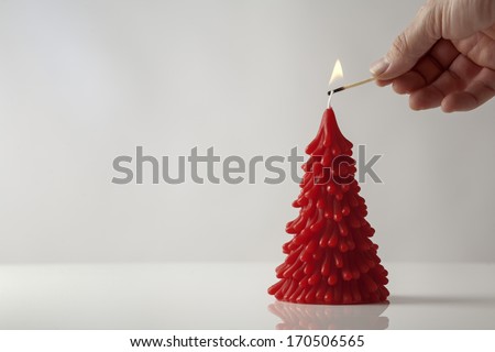 mans hand holding a match lighting a candle in the shape of a christmas tree