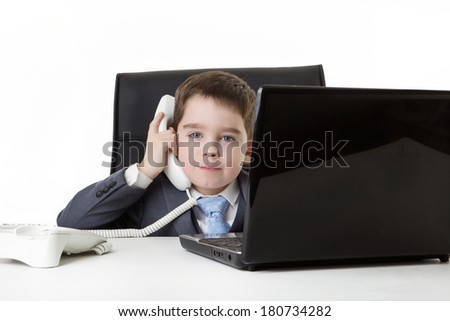 young small boy pretending he\'s working in a office on a laptop computer and answering the phone