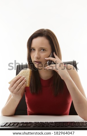 woman sitting at her desk in the office eating a sandwich as well as working on the go