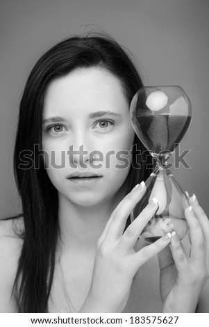 head shot of a young woman shot in the studio looking into camera model is holding a large sand timer