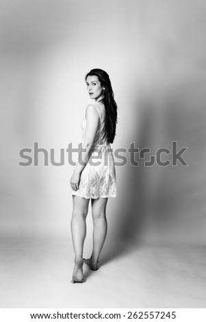 black and white image of woman shot in the studio standing and walking away looking back round at the camera wearing a lace dress
