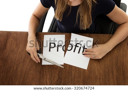 woman shot from above cutting paper in half with the word profit written on the paper