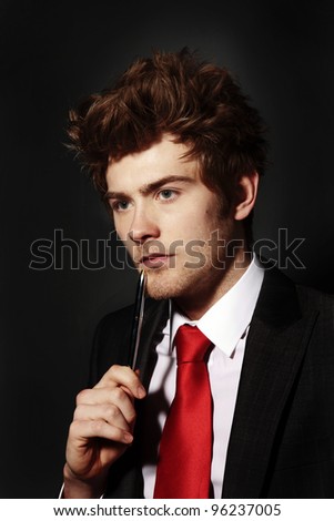 low key image of a young businessman holding a pen up to his face