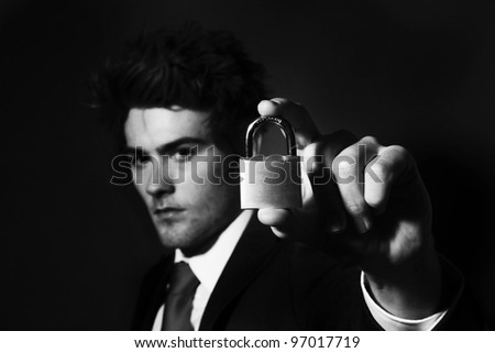 low key portrait image of businessman holding up a pad lock