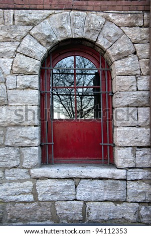 Beautiful red window or door in old stone wall with steel security bars and reflections of trees