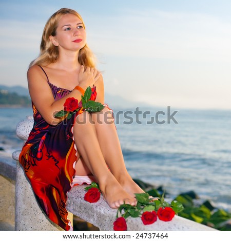 Young woman with rose flowers near the ocean at sunrise time