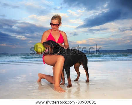 Woman playing with dog near the ocean at sunset time