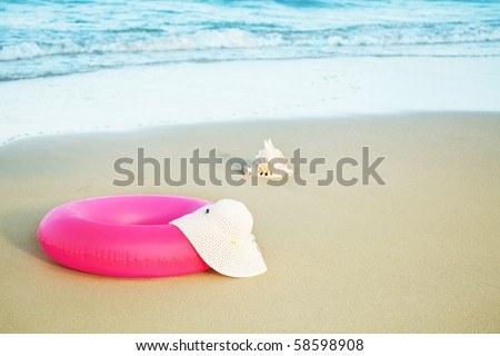Seashell, inflatable tube and hat on sand