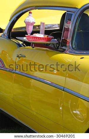 Old restored yellow automobile at oldies car show with fake food on a tray to simulate a drive thru restaurant.