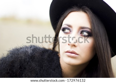 Outdoor fashion portrait of elegant brunette looking away. Dressed with elegant black sweater and black hat
