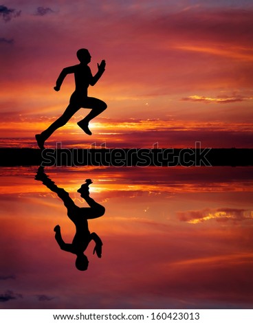 Silhouette of running man on sunset fiery background. Silhouette of man running at sunset. Water reflection. Element of design.