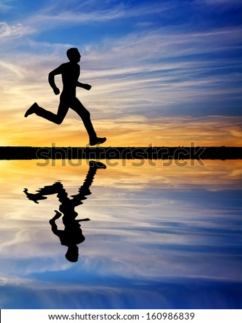 Silhouette of running man against the colorful sky. Silhouette of man running at sunset. Water reflection. Element of design.