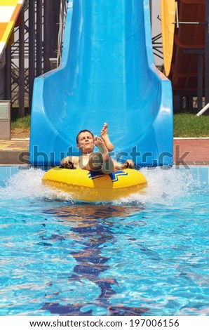 Men go down from water slide to swimming pool in aqua park. Happy men have fun on aqua park