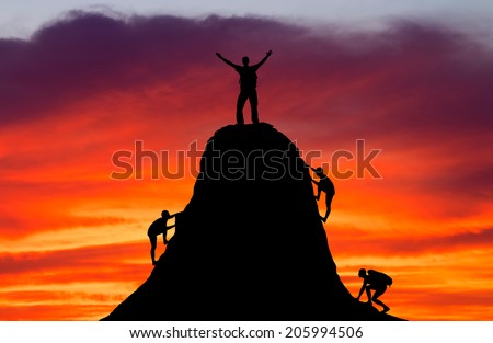 Man on top of the mountain and the other people to climb up on fiery orange background. Rock climber at sunset background. Sport and active life.